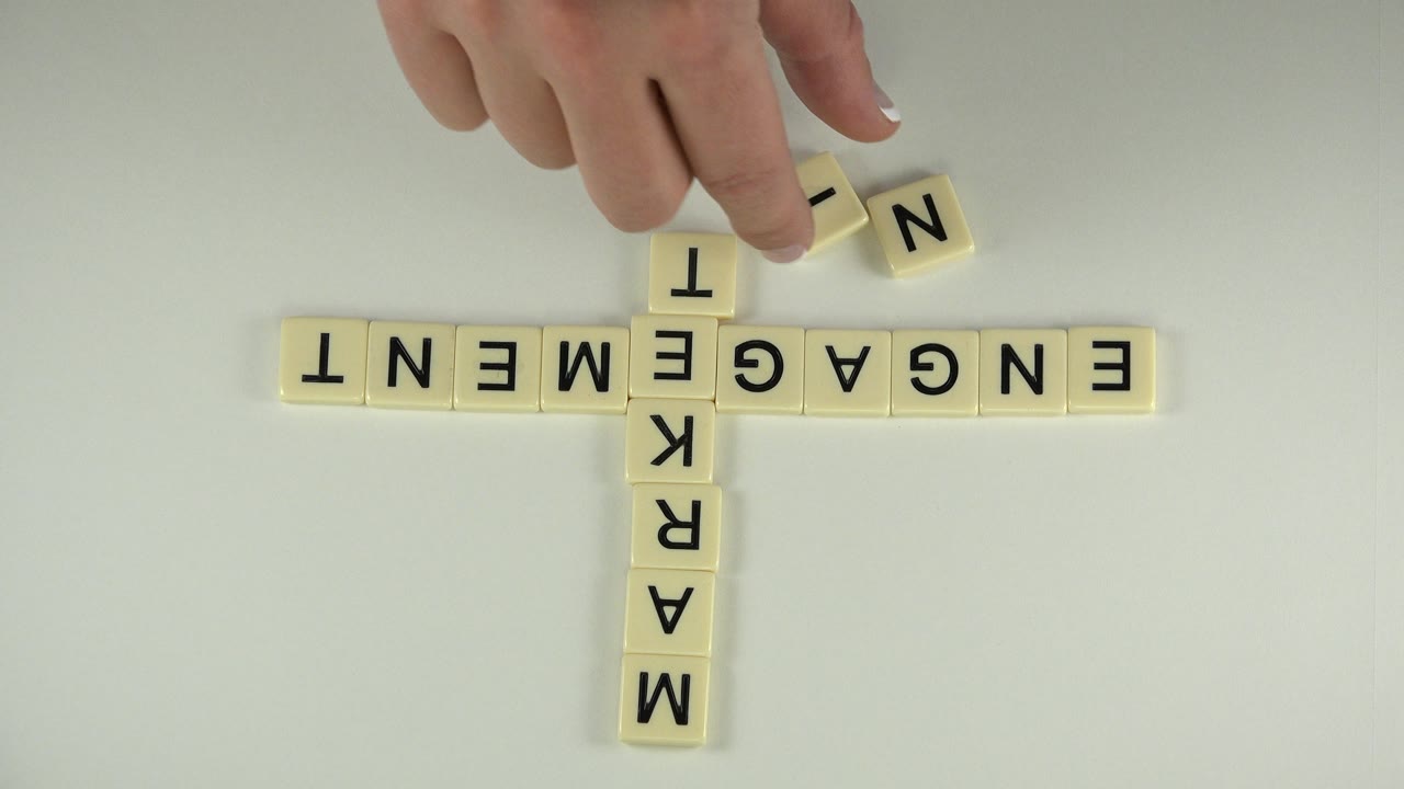 Hand nudging a tile near the upper end of a letter-block crossword.