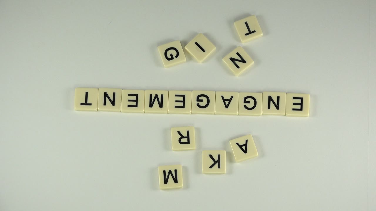 A static overhead frame in Westminster, Colorado shows the ENGAGEMENT tile row centered with loose G, I, N, T, M, R, K, and A tiles nearby and no visible people.