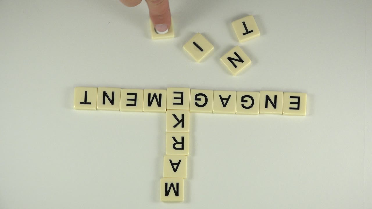 Manicured finger above cream letter tiles spelling ENGAGEMENT and MARKET.