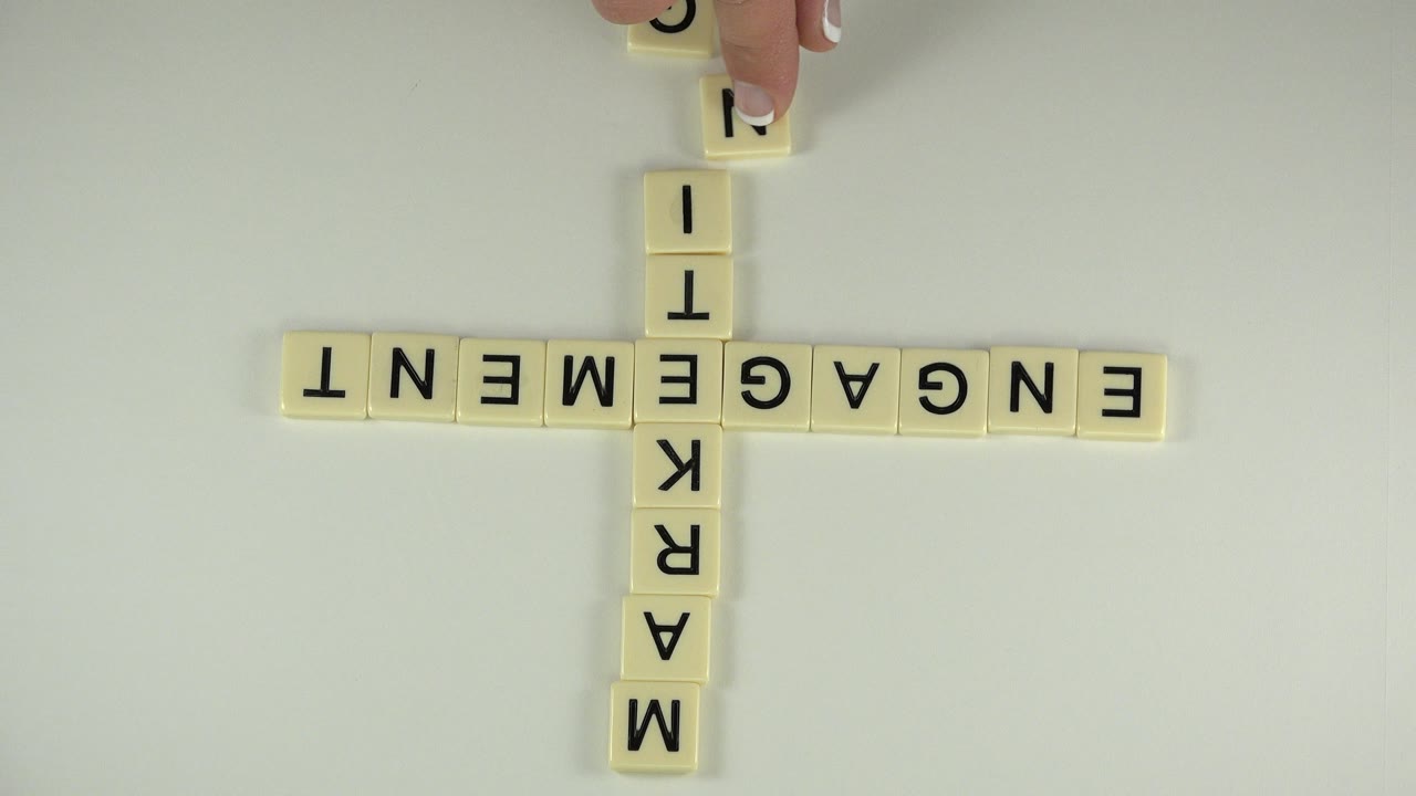 Overhead Westminster, Colorado frame of cream letter tiles arranged as a plus sign, with engagement across and marketing vertically on a pale tabletop.