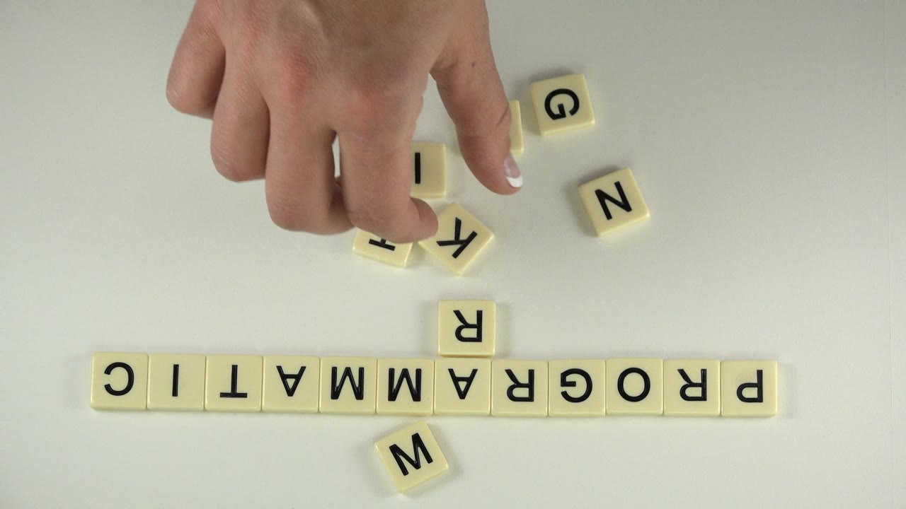Hand over cream letter blocks spelling PROGRAMMATIC on a pale tabletop.