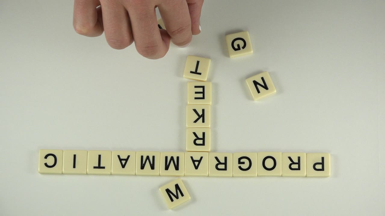Hand above letter tiles spelling programmatic and marketing on a pale tabletop.