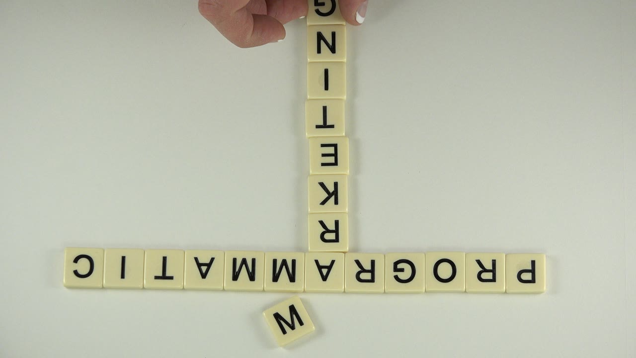 Overhead view of letter blocks on a pale tabletop with a hand at the top edge.