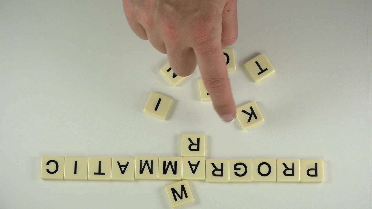 Hand reaching toward scattered letter tiles above a row spelling PROGRAMMATIC.
