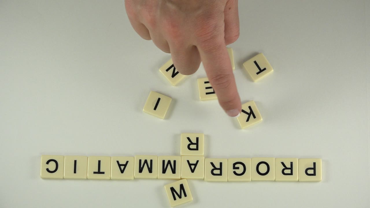 At 0:01 in Westminster, Colorado, a fingertip presses a K tile while loose letter tiles sit above the PROGRAMMATIC row.