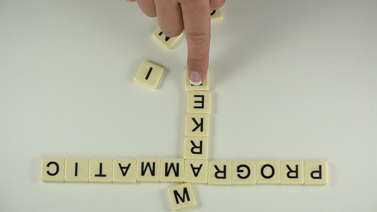 Overhead view in Westminster, Colorado, of cream letter tiles spelling PROGRAMMATIC while a fingertip presses near the start of a vertical word, with no visible faces.
