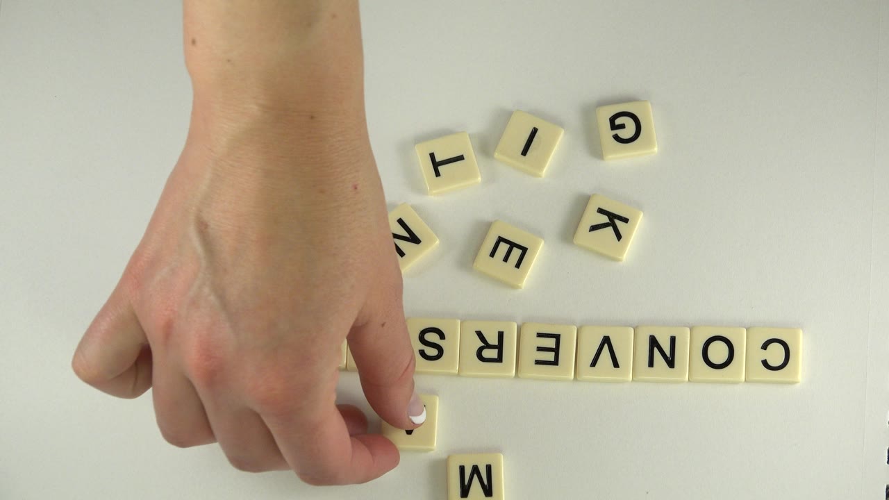 Hand above letter tiles spelling CONVERSATION on a pale tabletop.