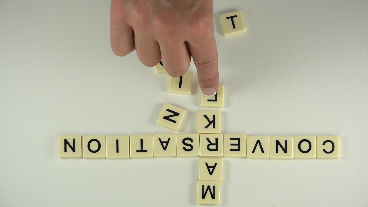 Hand pressing a letter cube beside alphabet blocks spelling conversation.