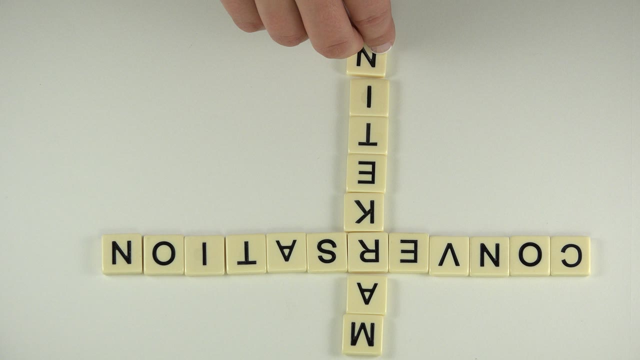 At 0:01 in the Westminster, Colorado clip, the tile cross stays centered as partial fingers touch the upper end of the vertical MARKETING word.