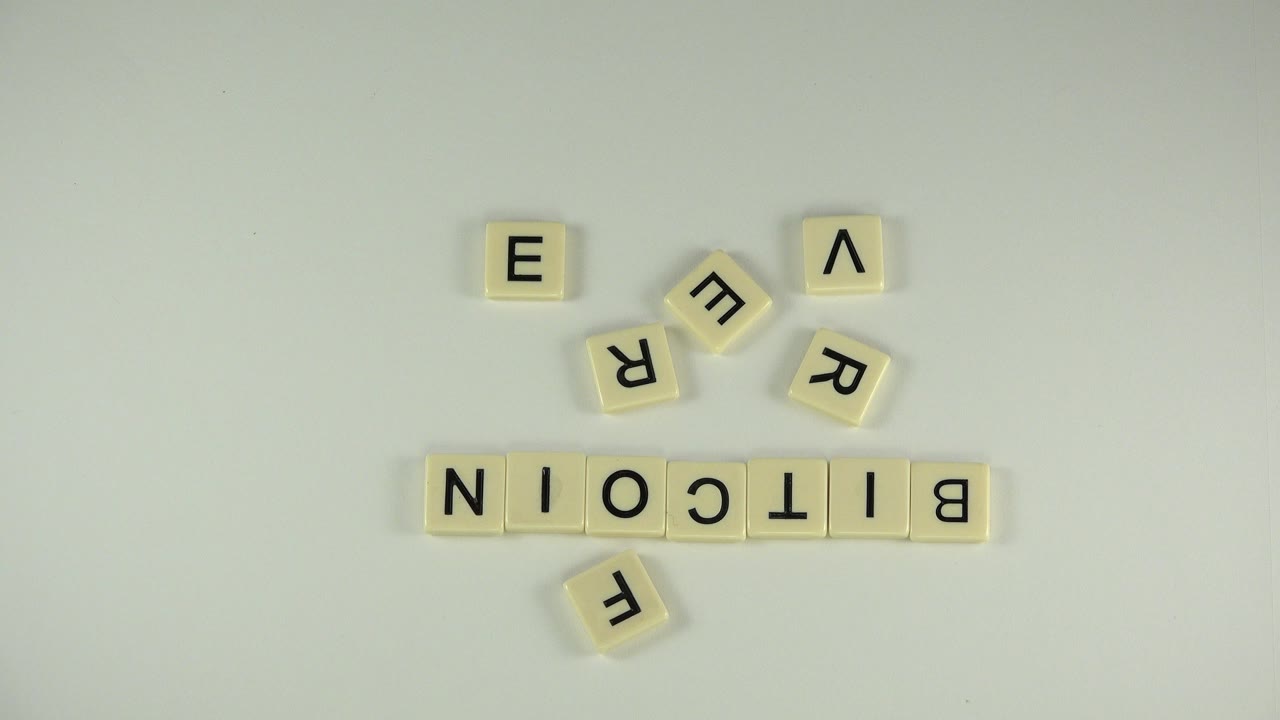 Overhead view in Westminster, Colorado of cream letter tiles spelling BITCOIN on a white tabletop, with loose letter tiles above and below and no visible people.