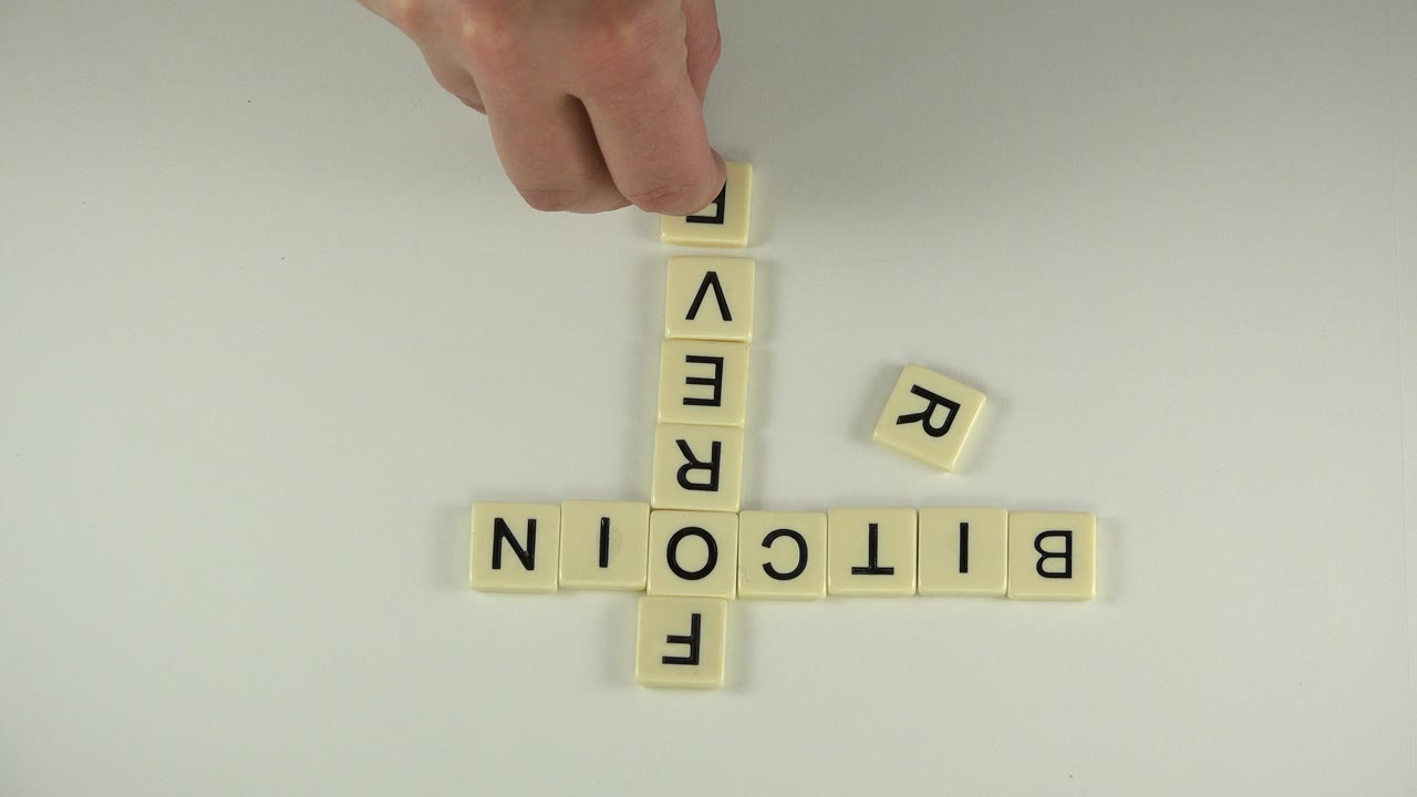 At 0:00 in Westminster, Colorado, letter tiles form BITCOIN across the table and FOREVER vertically, while a hand reaches in from the top with no visible face.