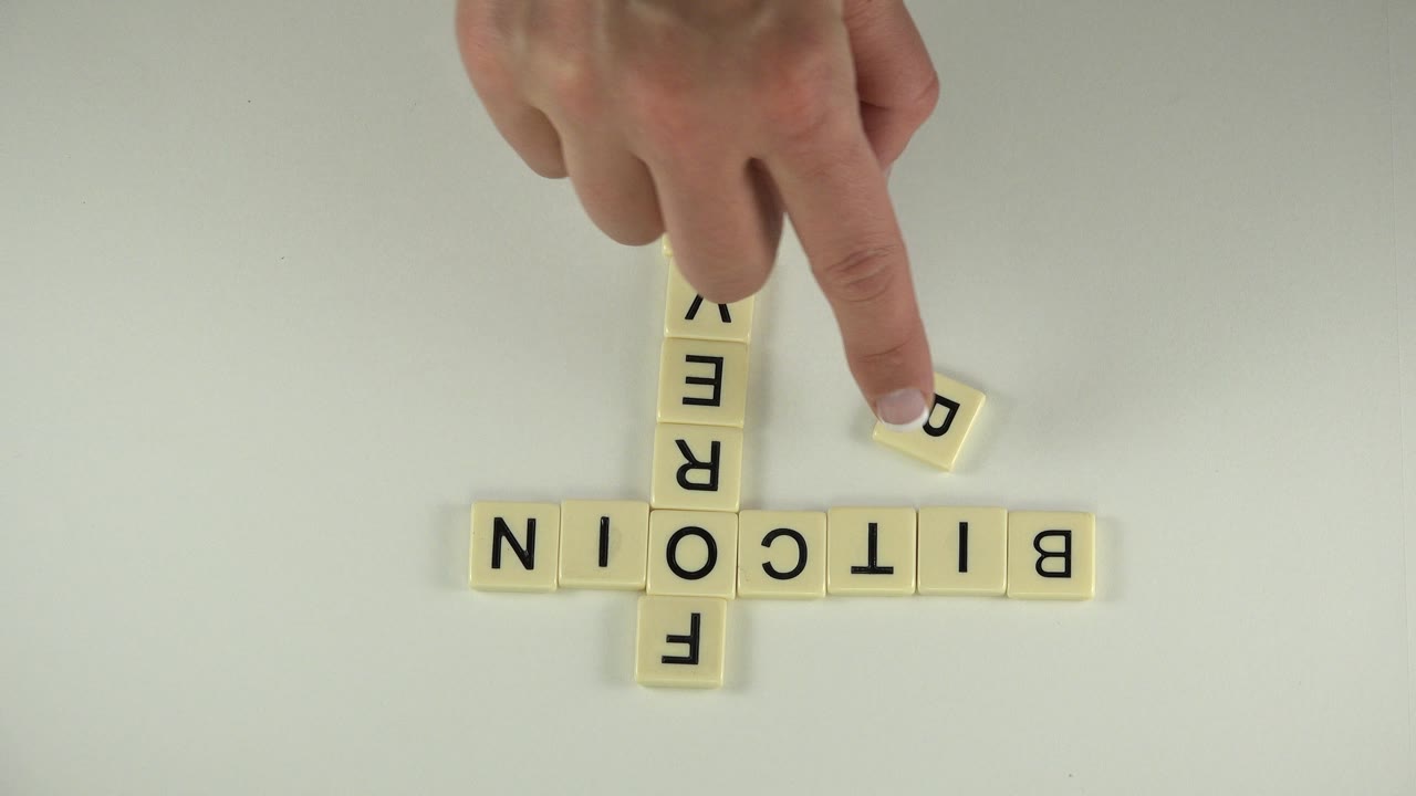 A finger points toward a loose letter tile beside the BITCOIN and FOREVER layout.