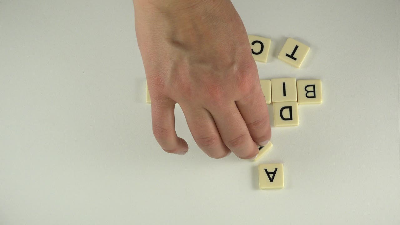 Hand placing cream letter tiles on a white table.