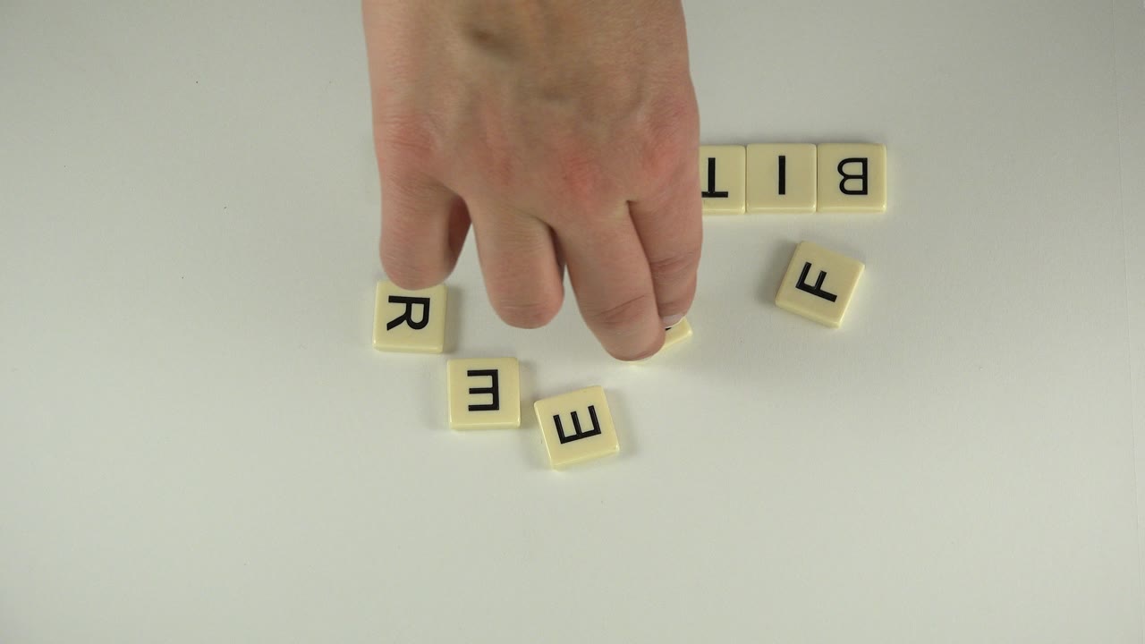 At 0:01 in Westminster, Colorado, the hand hovers over the tabletop as the letter tiles begin forming a partial word beside scattered pieces, with no visible face.