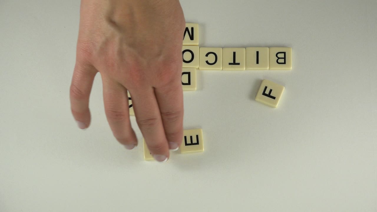 Hand near cream alphabet tiles on a pale tabletop.