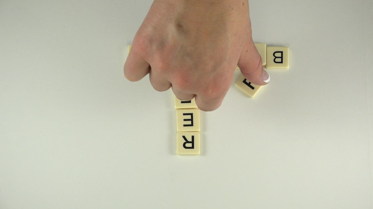 Hand placing letter tiles on a pale tabletop.