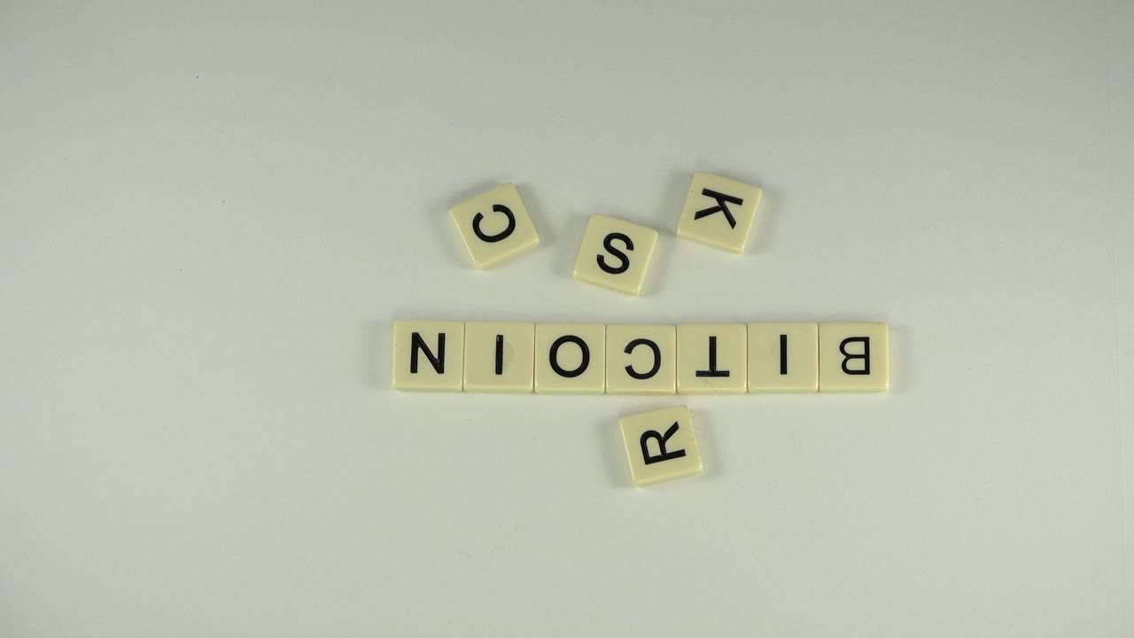 Letter tiles spelling BITCOIN on a pale surface with loose tiles above and below.