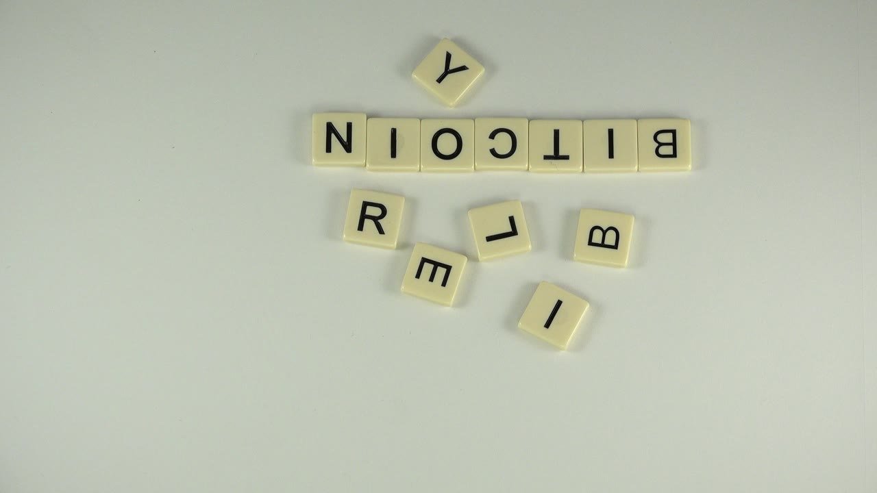 Letter tiles spelling Bitcoin with loose tiles below on a white surface.
