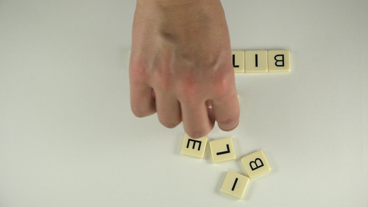 Adult hand hovers near loose B, L, and I tiles while a partial BIT tile row remains near the top of the overhead frame in Westminster, Colorado.