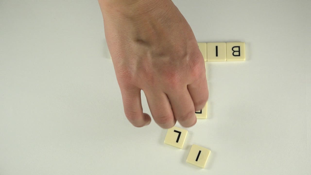 Hand reaching toward loose cream letter tiles on a pale tabletop.