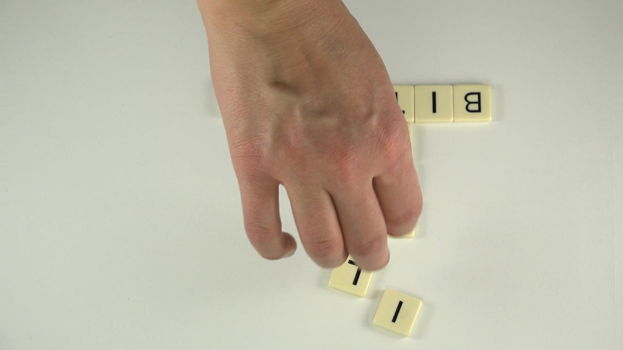 One second in, the hand moves a cream tile near a small group of black-letter tiles on the pale tabletop in Westminster, Colorado.