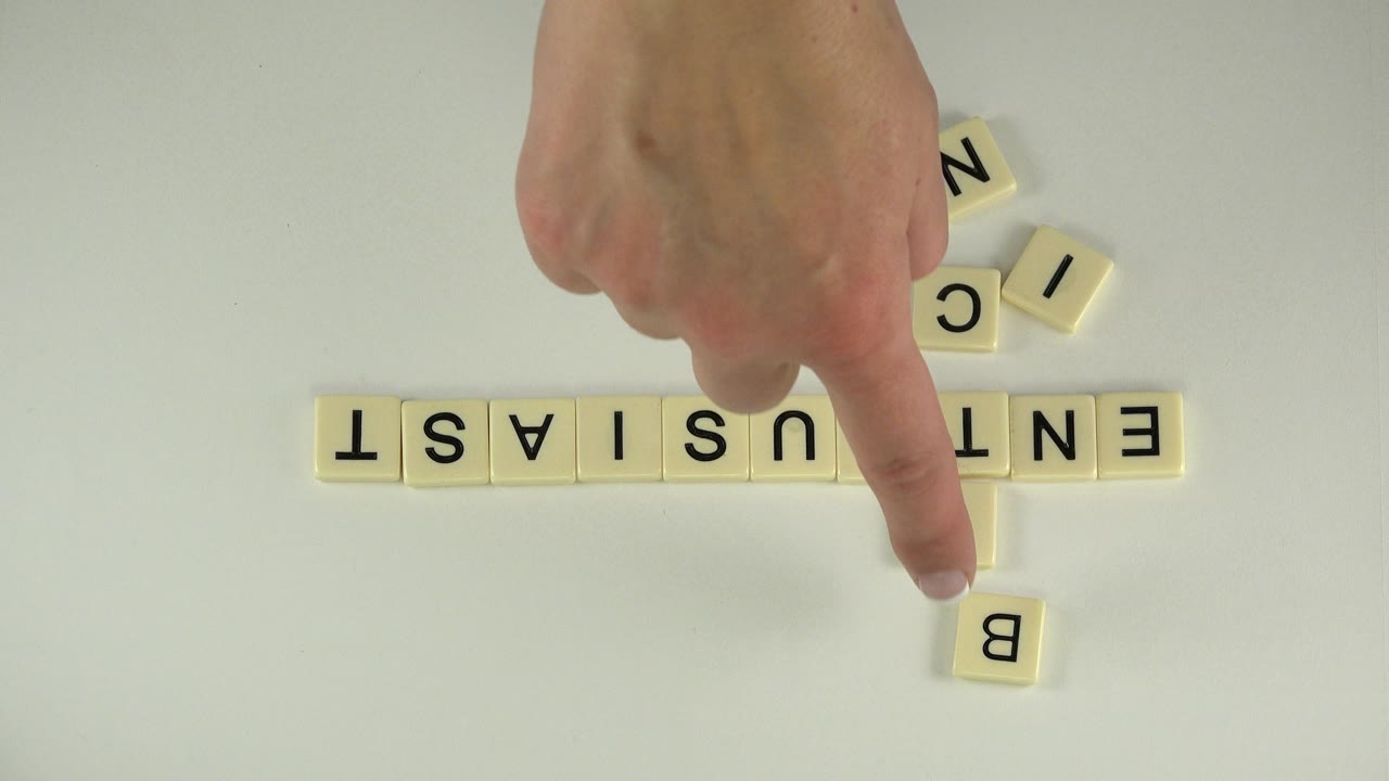 In Westminster, Colorado, a hand points near cream letter tiles as ENTHUSIAST runs horizontally and BITCOIN begins vertically on a pale tabletop.