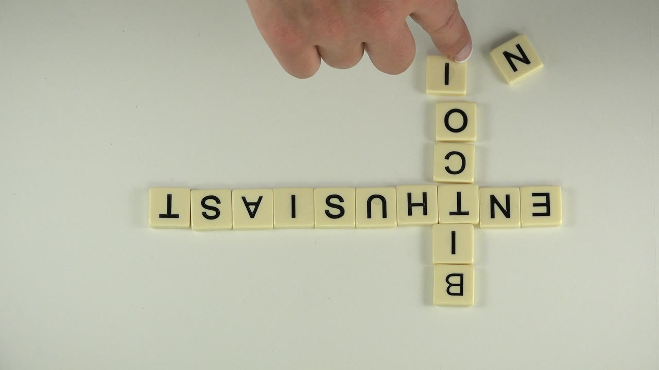 Hand placing letter tiles beside crossed word tiles on a pale table.