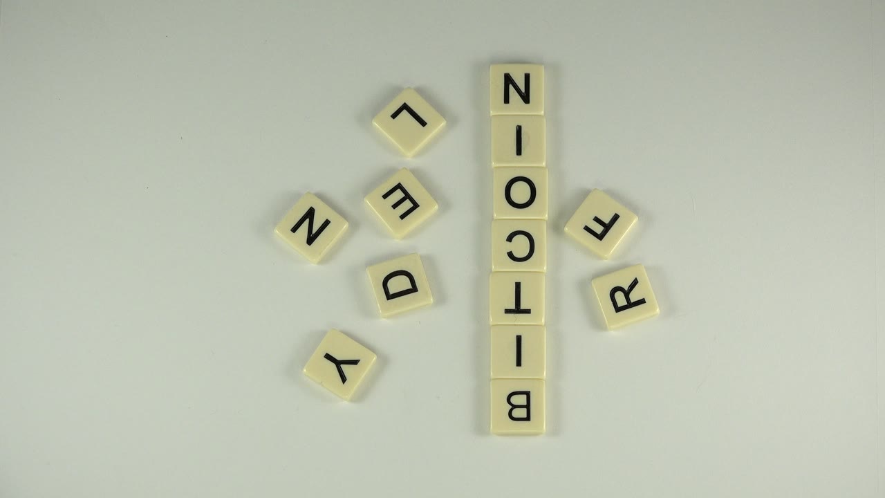 A nearly unchanged overhead view in Westminster, Colorado, holds on the vertical BITCOIN tile stack with scattered Y, E, N, D, V, and R tiles around it, no visible people.
