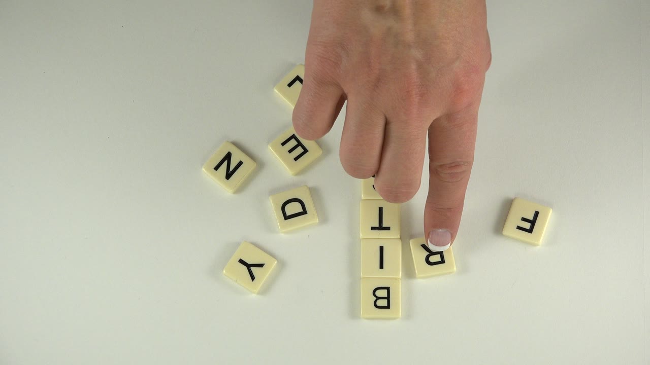 Hand placing cream letter tiles on a pale tabletop.