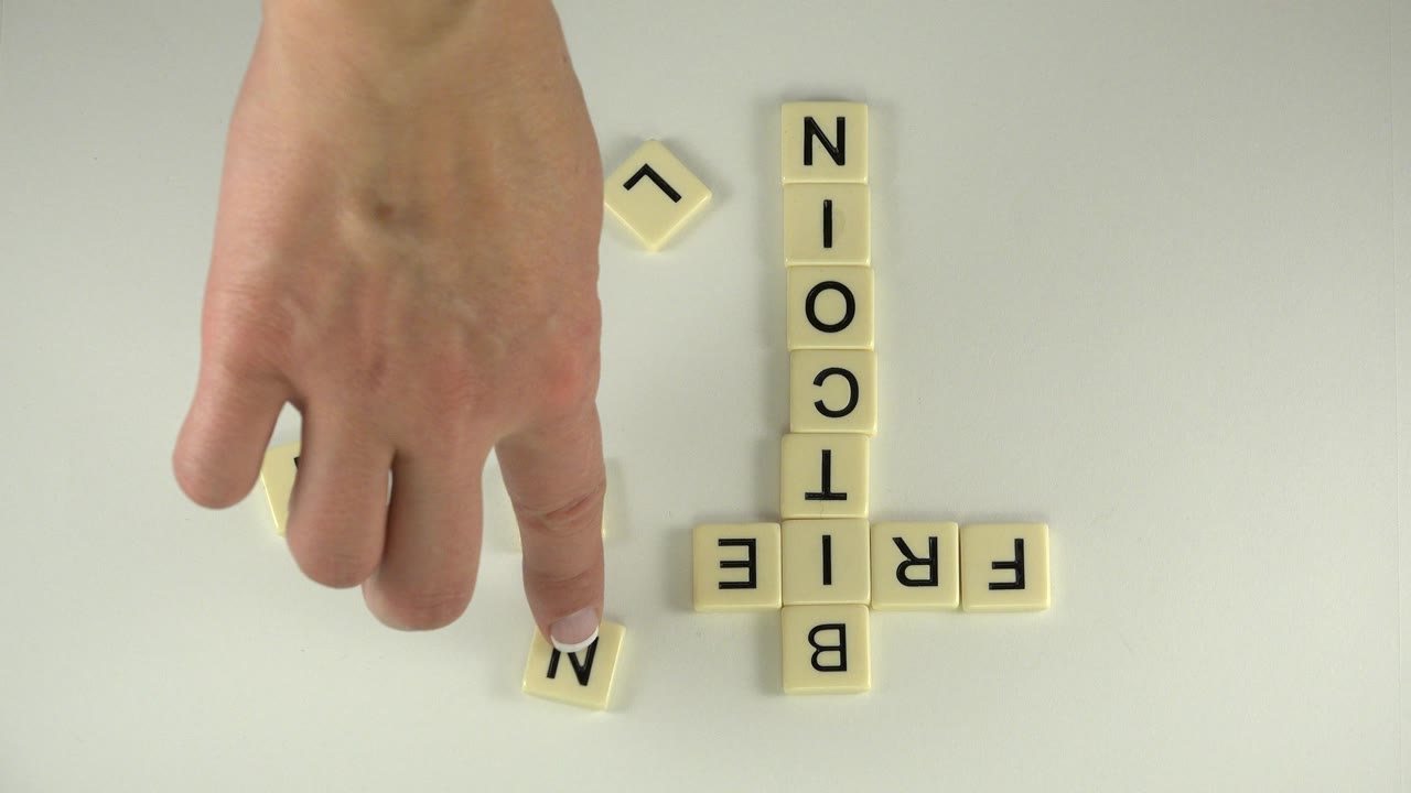 At 0:01, the hand presses a loose M tile near the completed vertical BITCOIN word and horizontal FRIEND word on the tabletop.