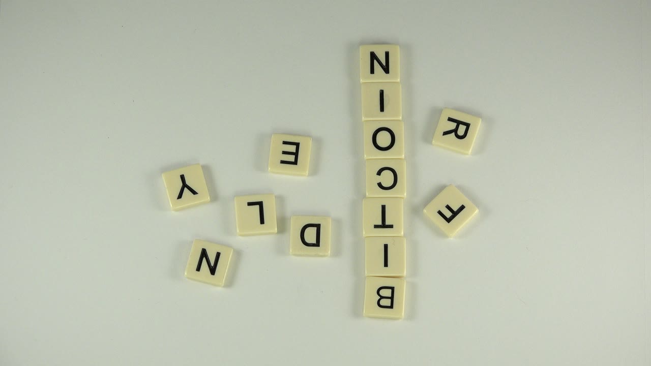 In Westminster, Colorado, cream letter tiles spell BITCOIN vertically on a pale tabletop, with loose tiles nearby and no visible people.