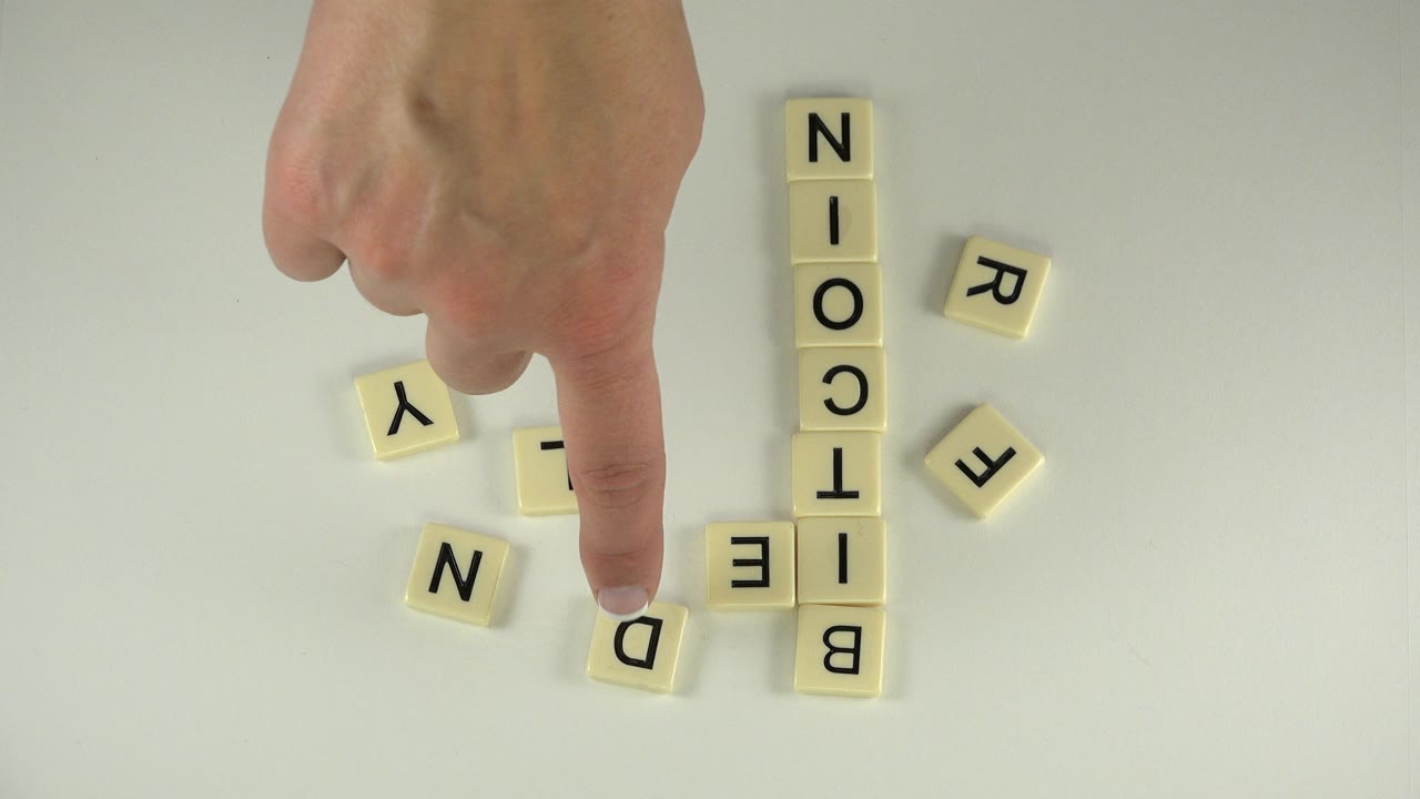Hand pointing near cream letter tiles on a tabletop.