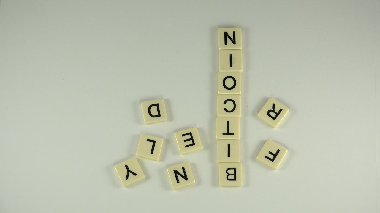 Letter tiles spelling BITCOIN on a pale tabletop with loose tiles nearby.