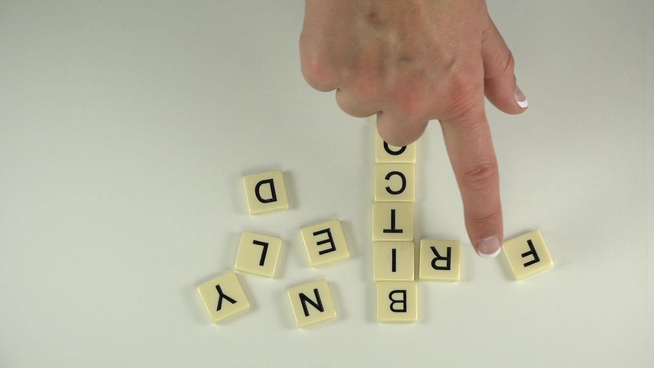 Hand pointing near letter tiles spelling Bitcoin on a tabletop.