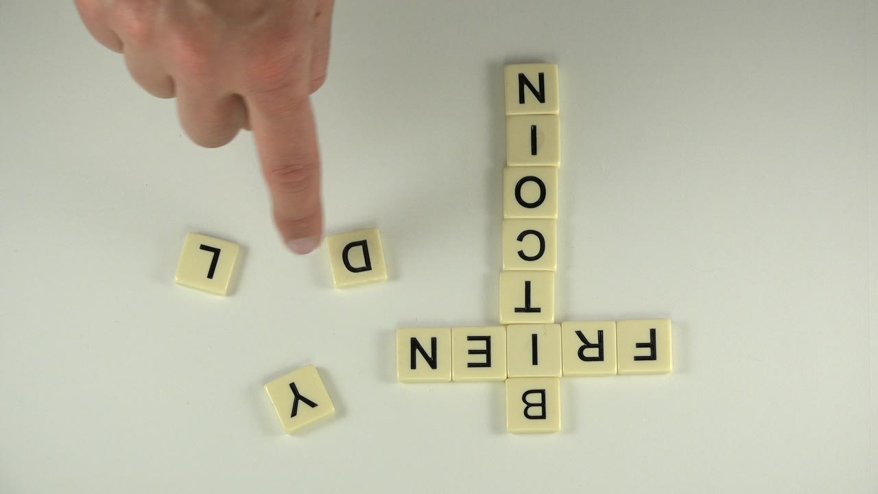 Hand points near loose letter cubes beside bitcoin and friendly tile words.
