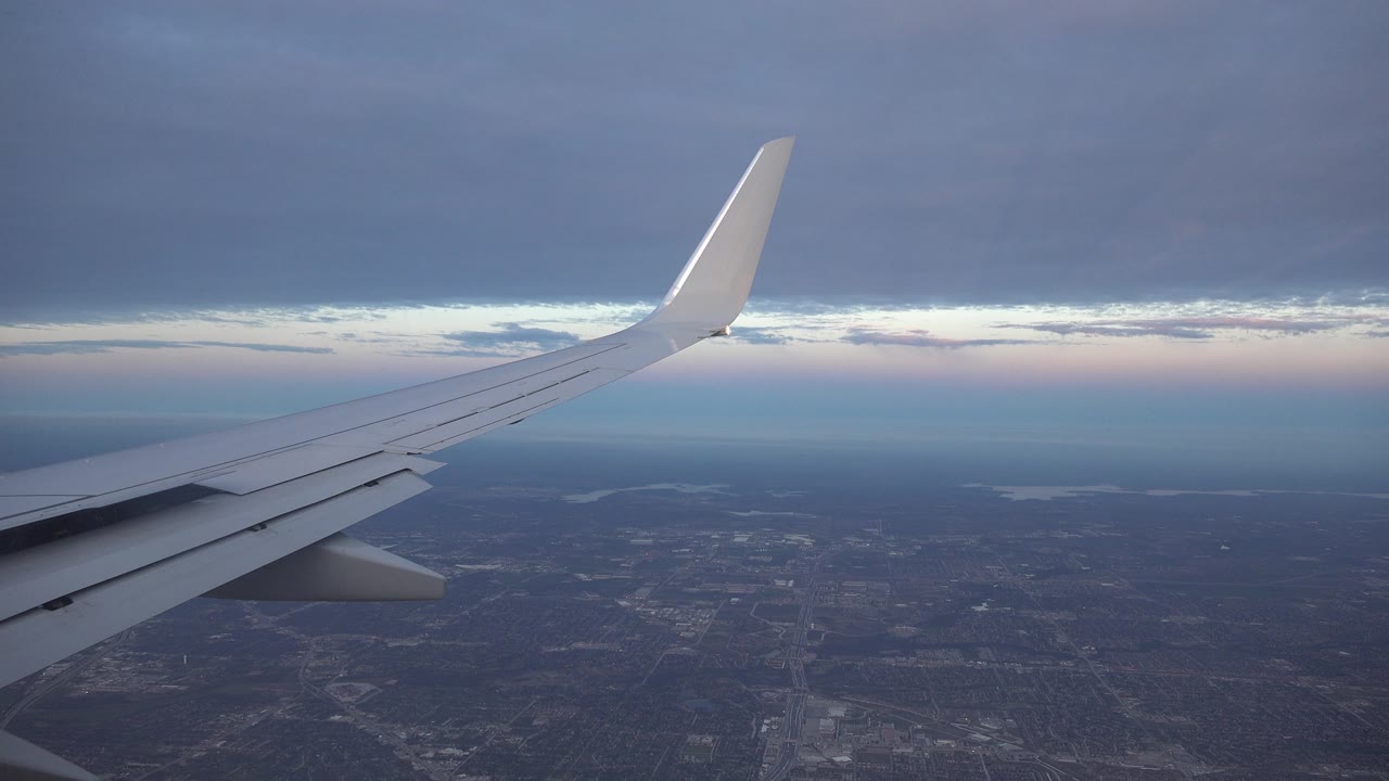 Airplane wing seen above land with a dark cloud ceiling.