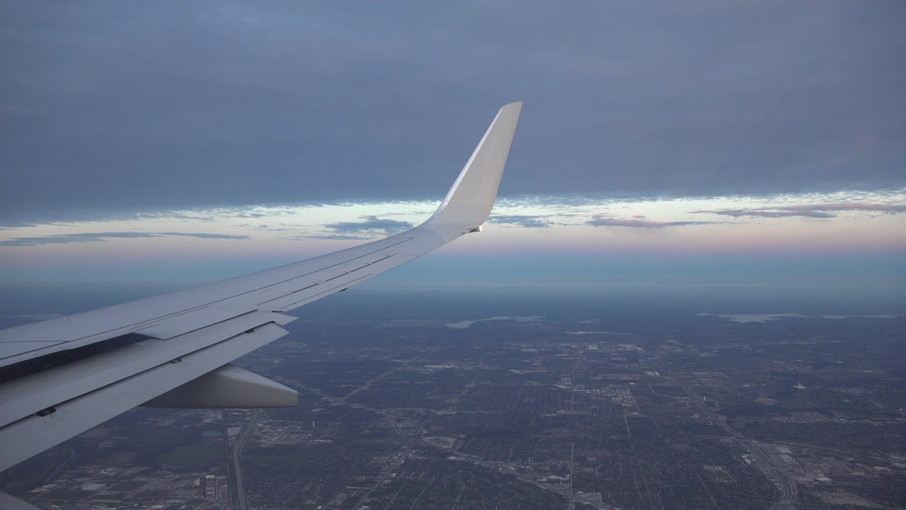 Airplane wing above a dark city grid under heavy clouds.