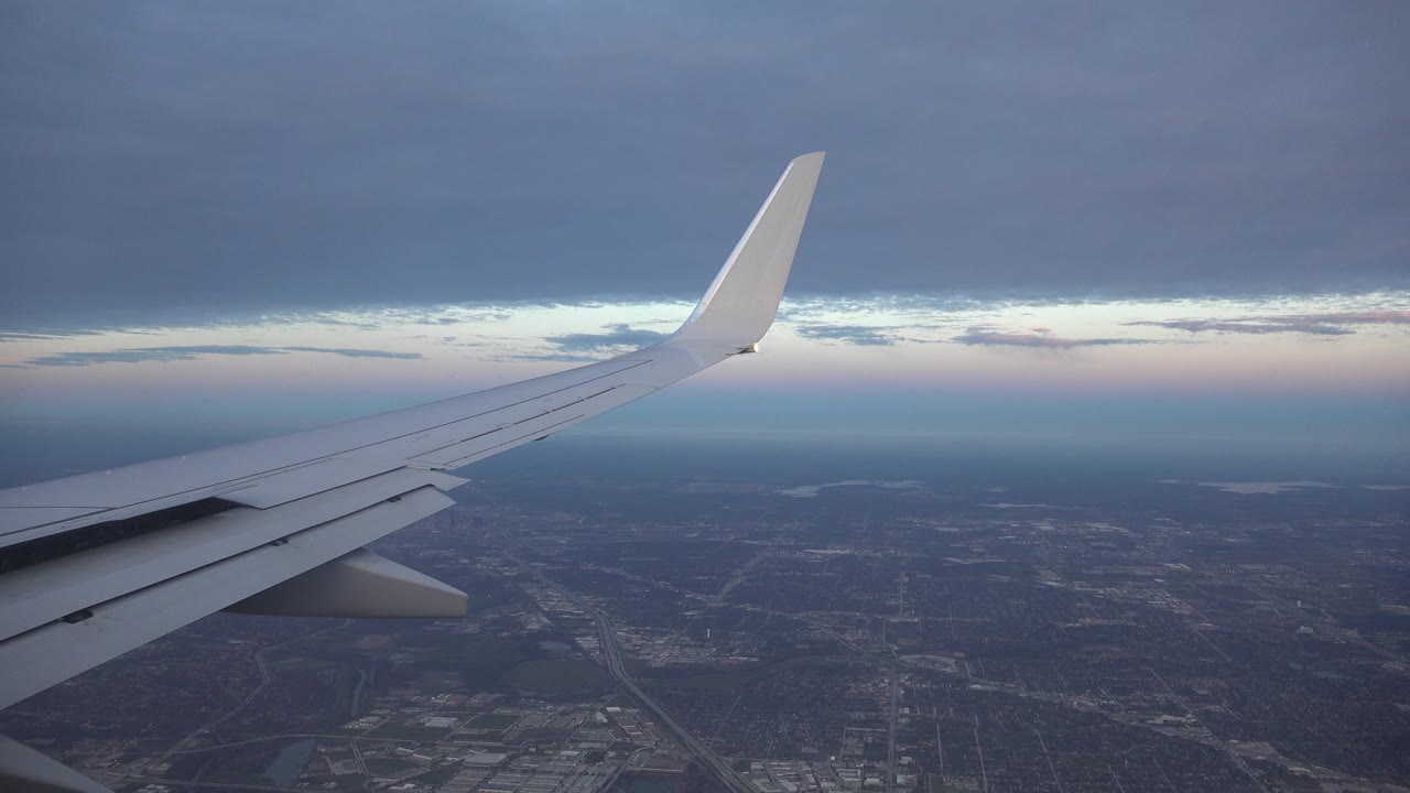 White airplane wing seen from a passenger window over lowland terrain near Playa del Carmen, Mexico, with dark clouds and no visible people.