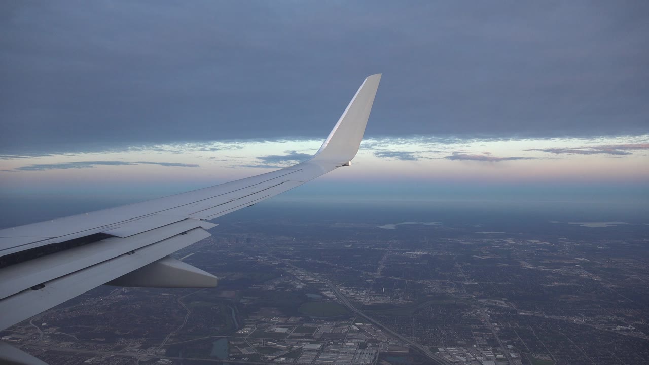 Aircraft wing over distant city and low clouds.