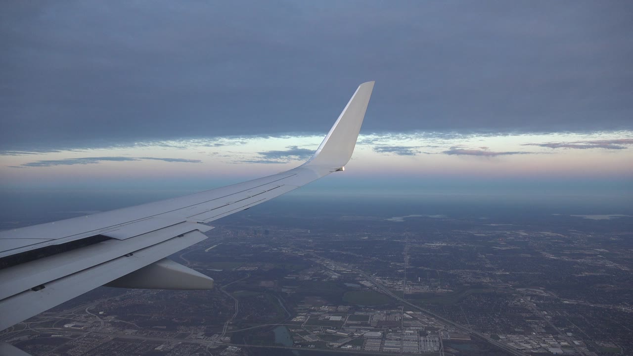 Airplane wing over dark land beneath blue-gray clouds.