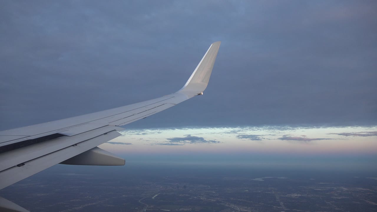Airplane wing over dark terrain and a narrow bright sky band.