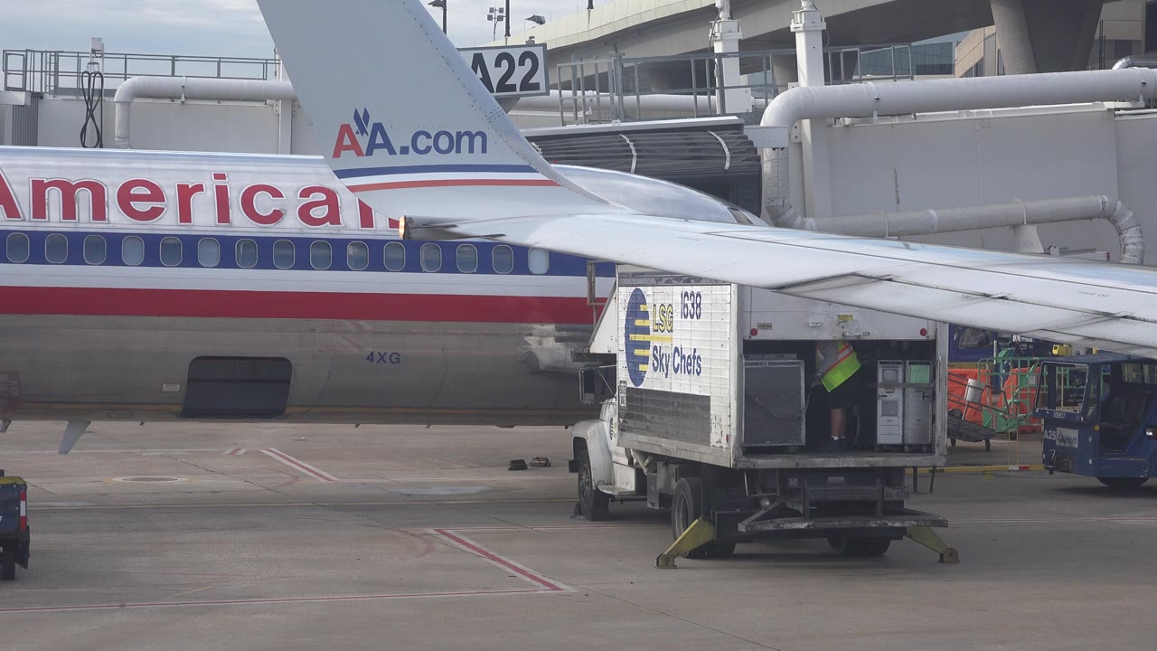 A similar airport ramp view in the Playa Del Carmen Mexico 2015 clip shows the American Airlines lettering partly cropped behind the wing, with the Sky Chefs truck centered and no visible people.