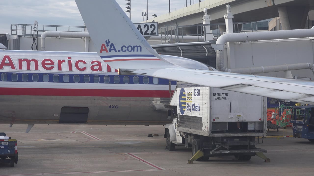 Airliner fuselage, tail, wing, and catering truck beside a terminal gate.
