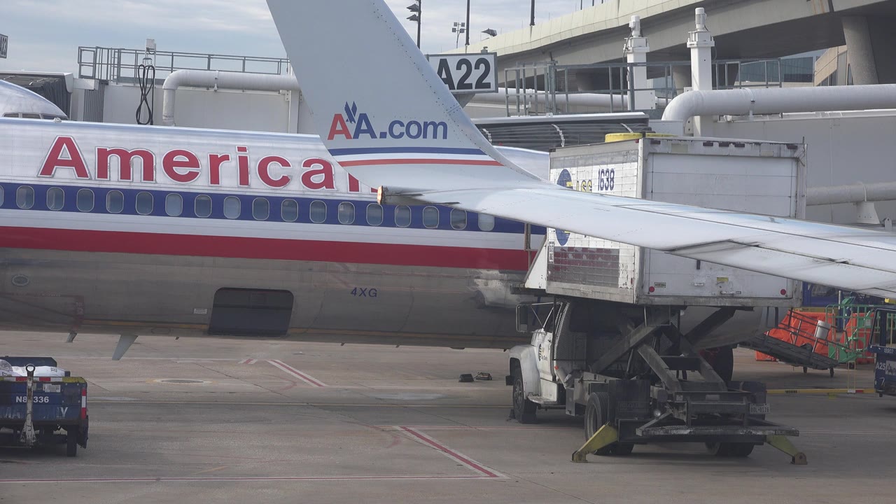 American Airlines jet at a gate with wing, jet bridge, and ramp equipment.