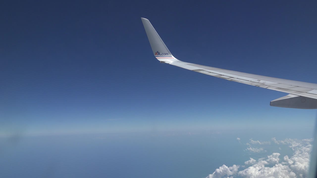 Passenger airplane wing over blue sky and scattered white clouds near Playa del Carmen, Mexico, with no visible people.