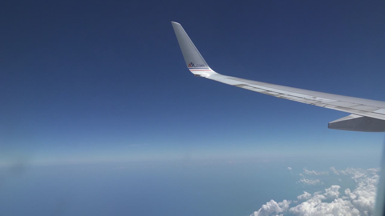Airplane wing stretches across the upper frame over a blue horizon and low clouds, recorded in the Playa del Carmen Mexico collection with no visible people.