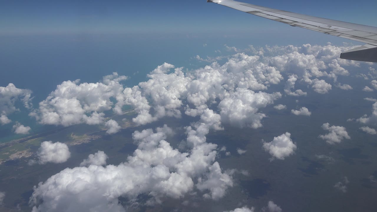 Airplane wing over scattered clouds and distant horizon.