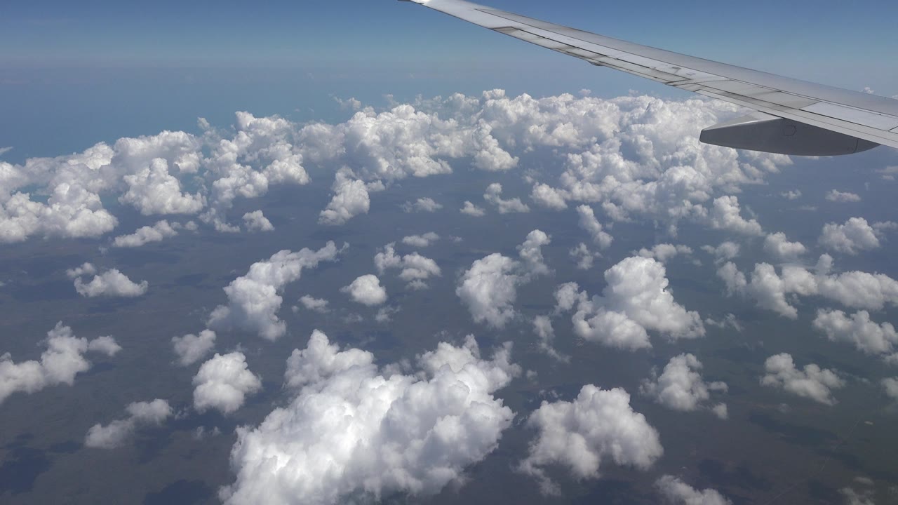 Airplane wing above scattered clouds and distant horizon.