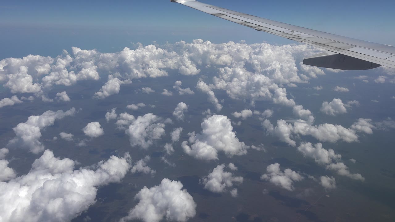 Plane wing over broken clouds and hazy blue horizon.