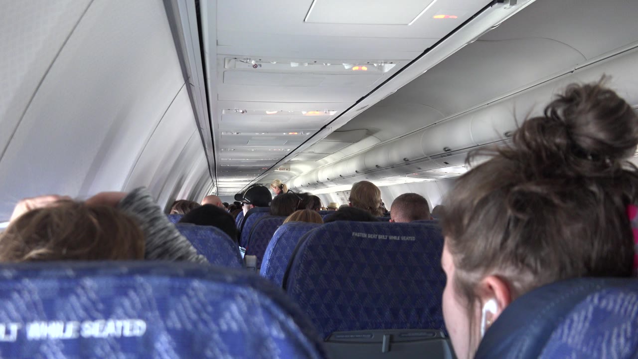 Airplane cabin with blue seatbacks and passengers ahead.